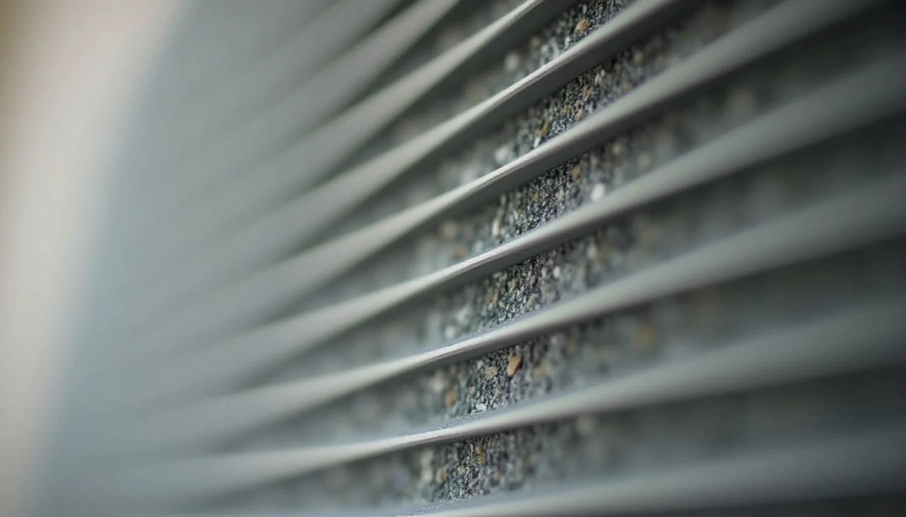 gray metal air conditioner fins layered horizontally with dust and debris accumulated between them