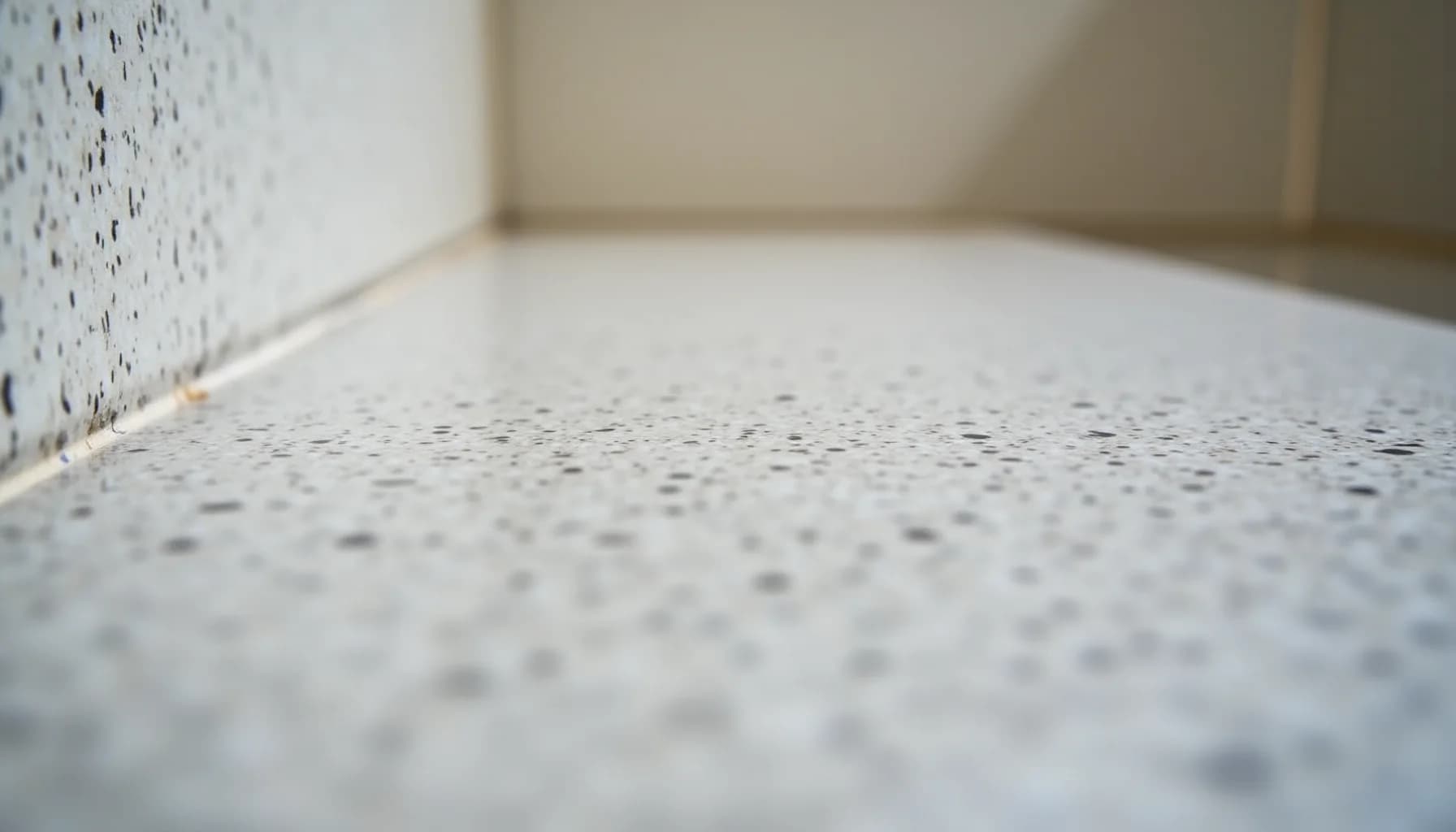 white speckled floor tile with dark flecks meeting a white textured wall in an interior corner