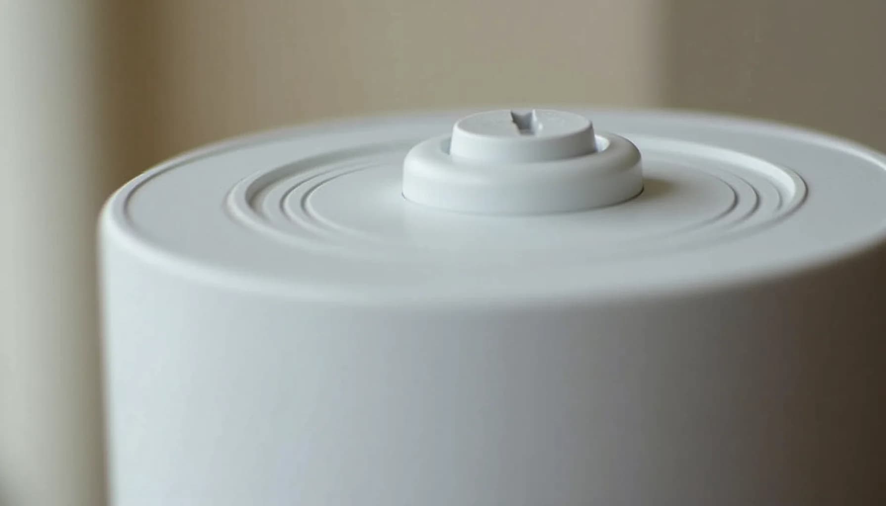 White cylindrical humidifier with concentric circular ridges on top surface and a small white cap with gray toggle