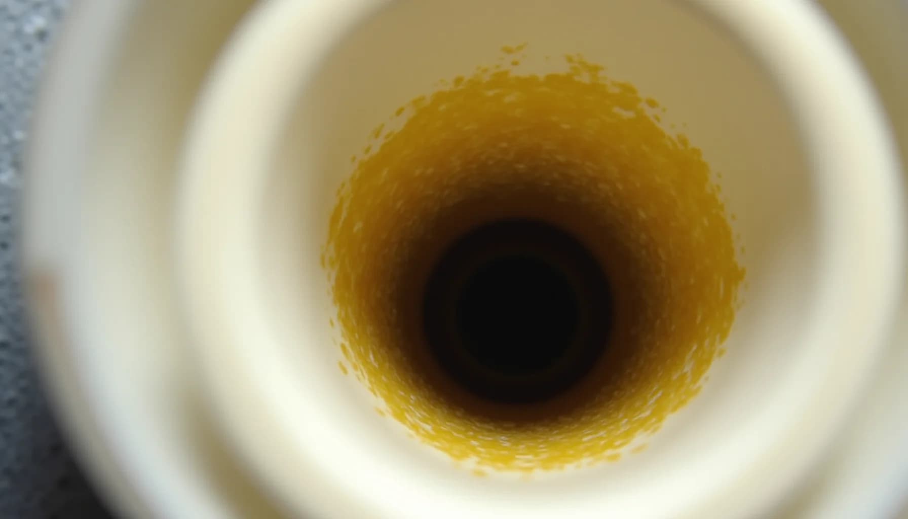 a kitchen sink drain opening with yellow-brown mineral deposits and buildup around the rim, surrounded by white