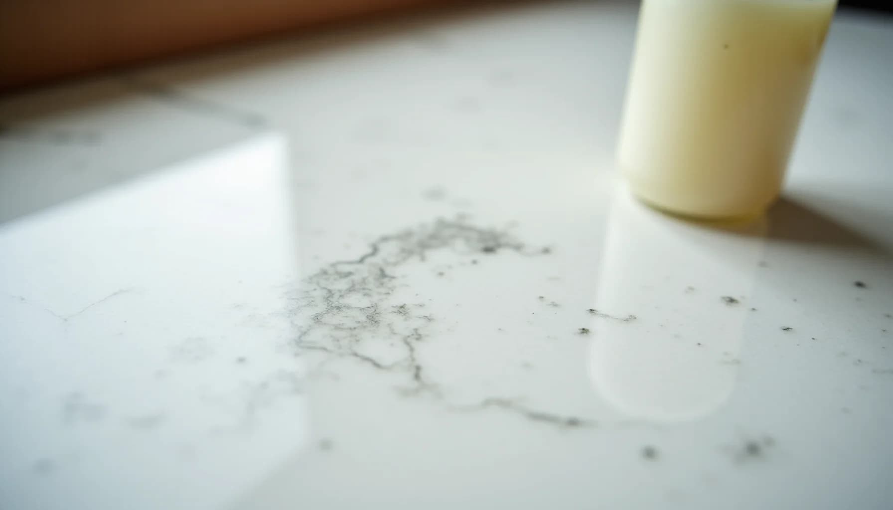 White marble countertop with spilled liquid and scattered debris, cream-colored bottle and white cloth visible nearby