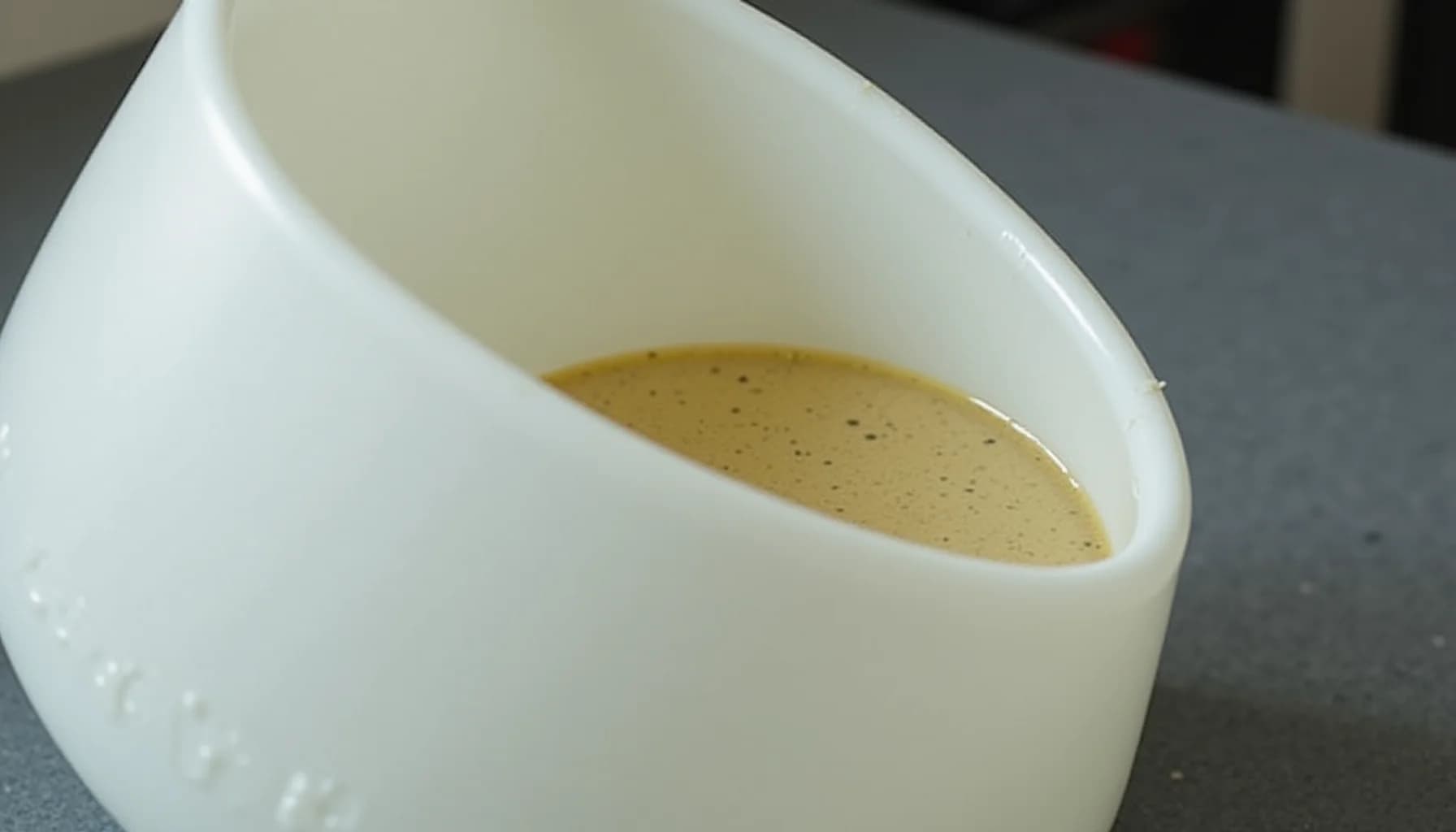 White ceramic cup containing tan liquid with sediment particles, shown at an angle on a gray surface