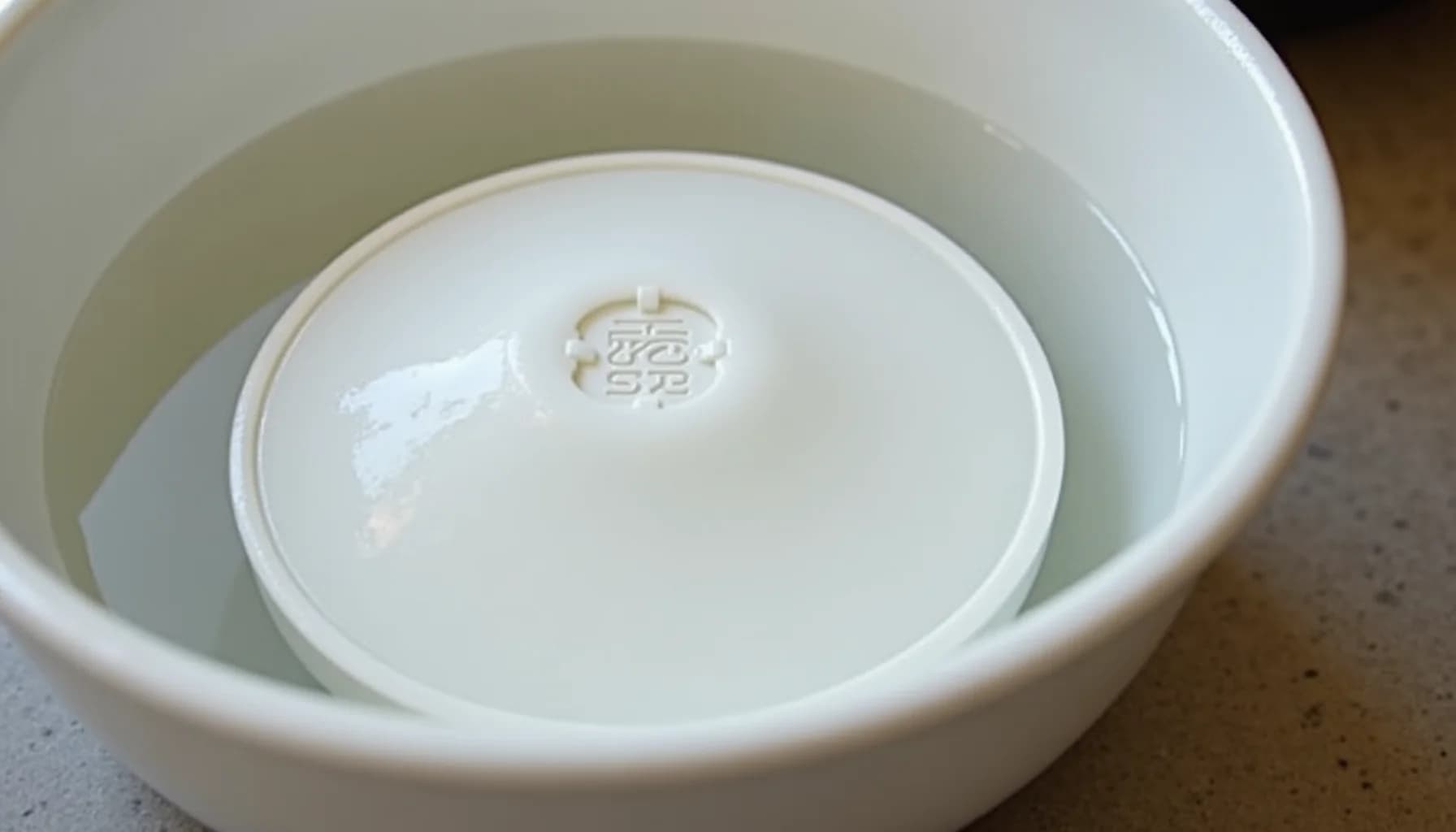 White ceramic bowl nested inside a larger white plastic basin containing clear water, with Asian characters embossed on