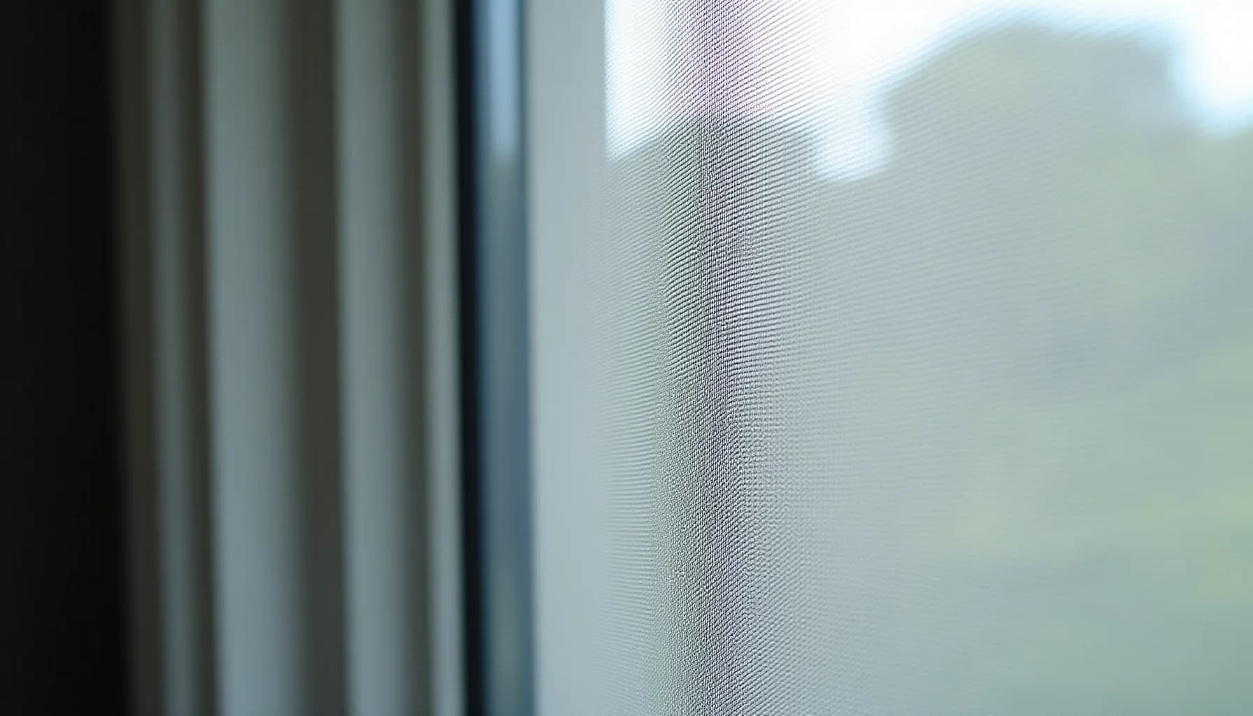 window screen mesh with metal frame, showing the fine mesh texture and window frame edge with soft light