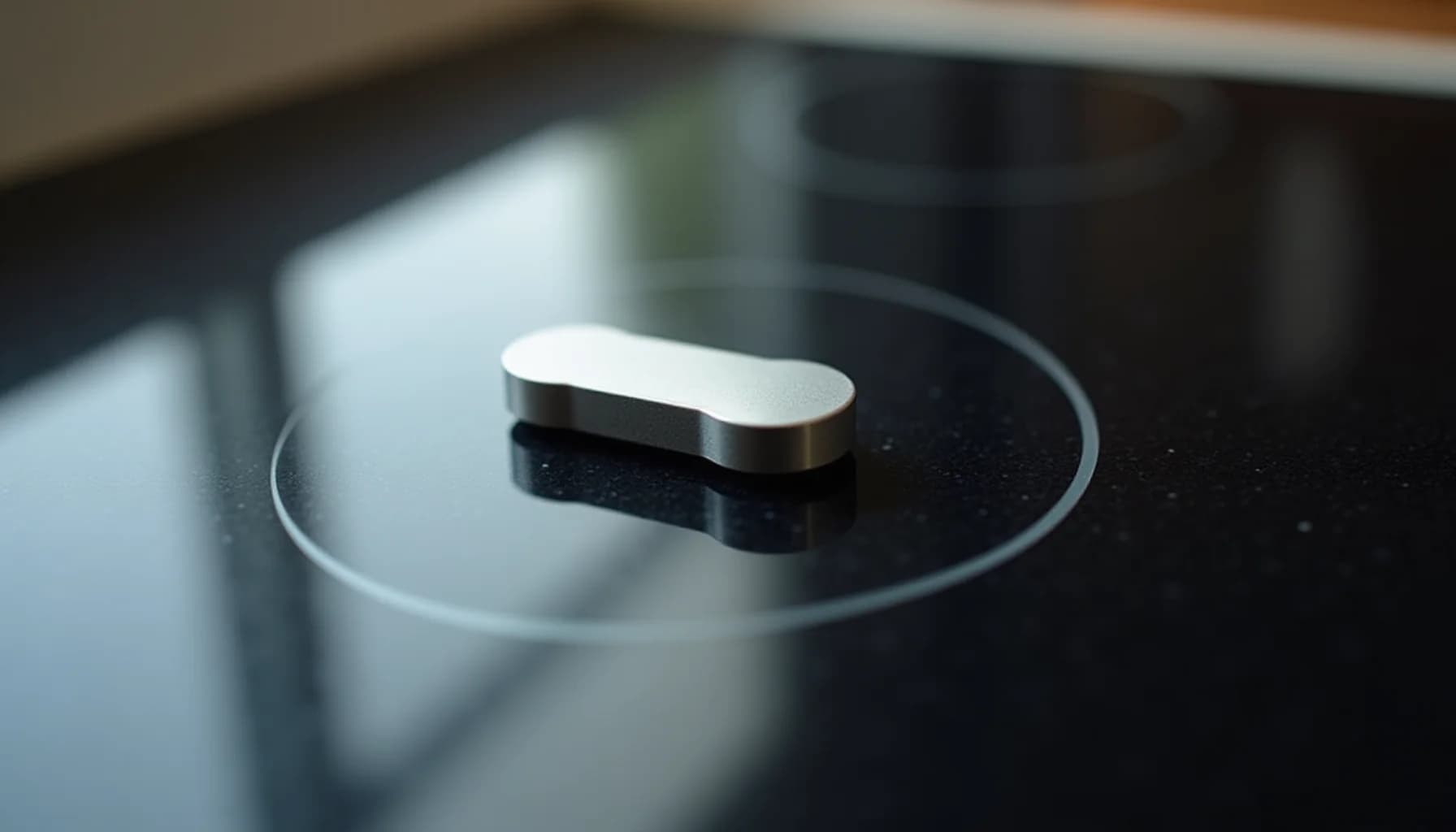 Silver metallic knob or control piece placed on a black glass cooktop surface with blurred background
