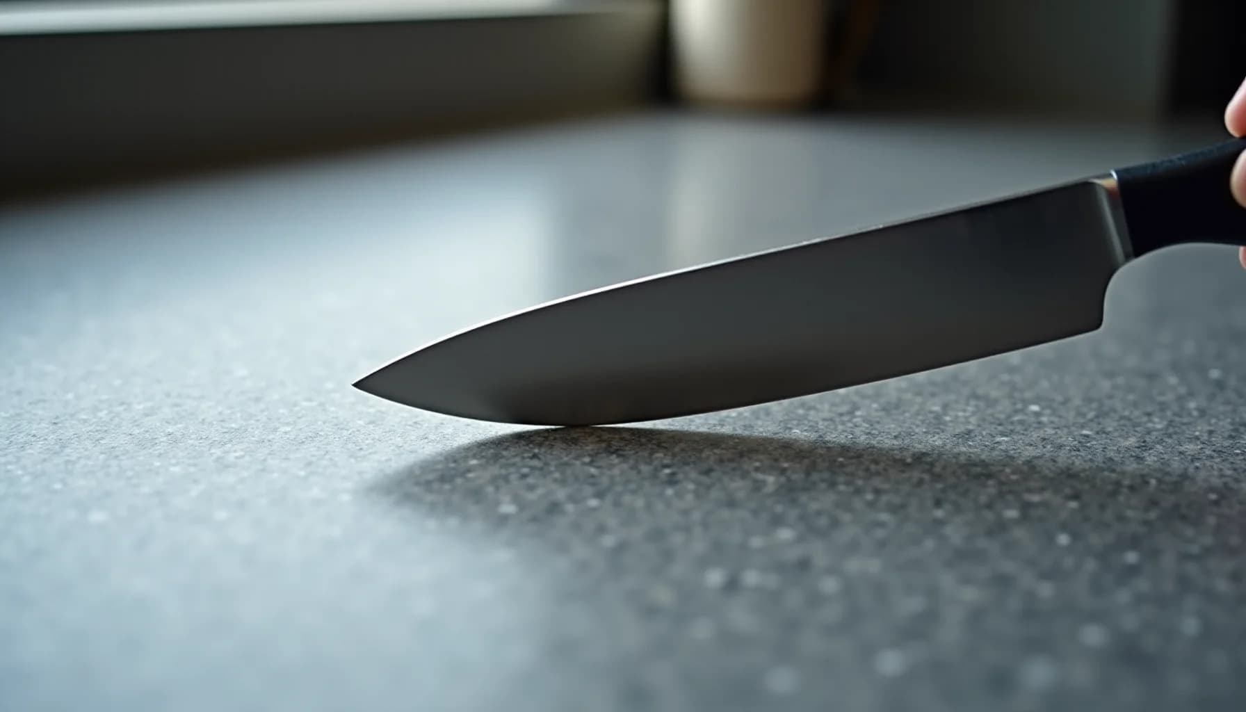 Black-handled chef's knife resting on a light gray speckled stone countertop surface
