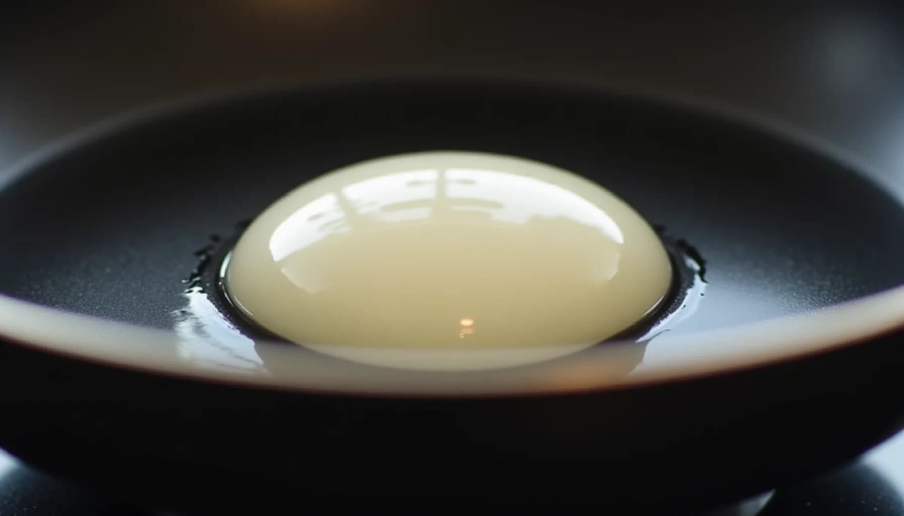 A raw egg with translucent white and pale yellow yolk sitting in a dark non-stick frying pan